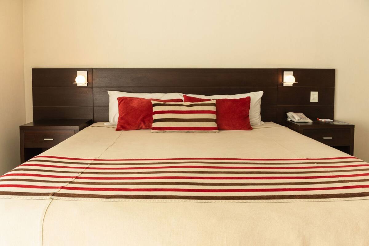 A bed with a striped blanket, two bedside tables with lamps, and a phone on one of the tables.