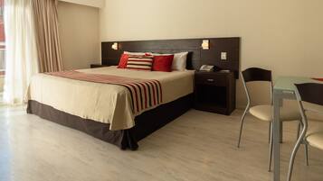 Una habitación de hotel con cama, mesita de noche, silla y escritorio con otra silla.