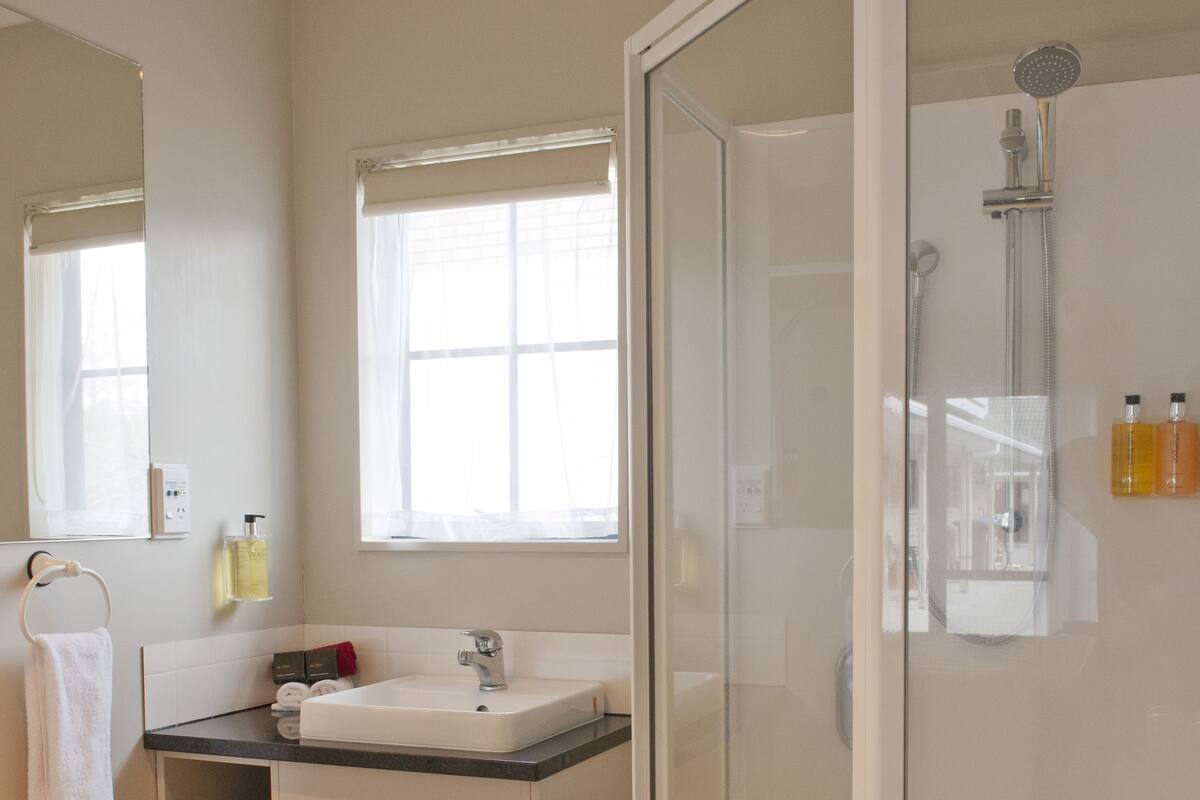 A modern bathroom with a glass-enclosed shower, a sink with a mirror, and a window providing natural light.
