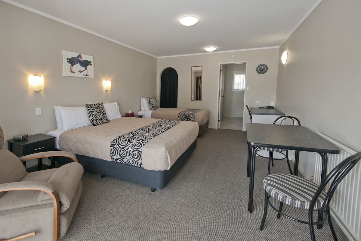 A hotel room with a double bed, a desk, a chair, a sofa, and a wall-mounted clock.