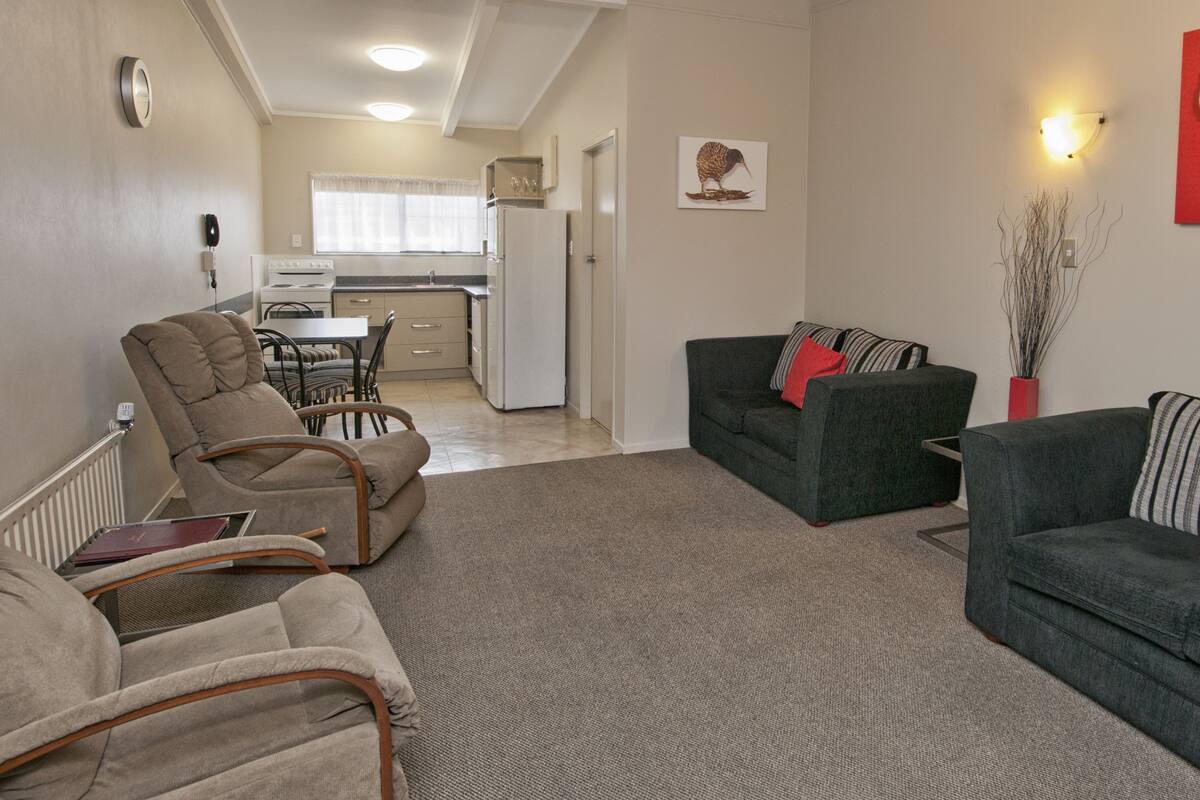 A living room with a sofa, armchair, and a dining area with a table and chairs.