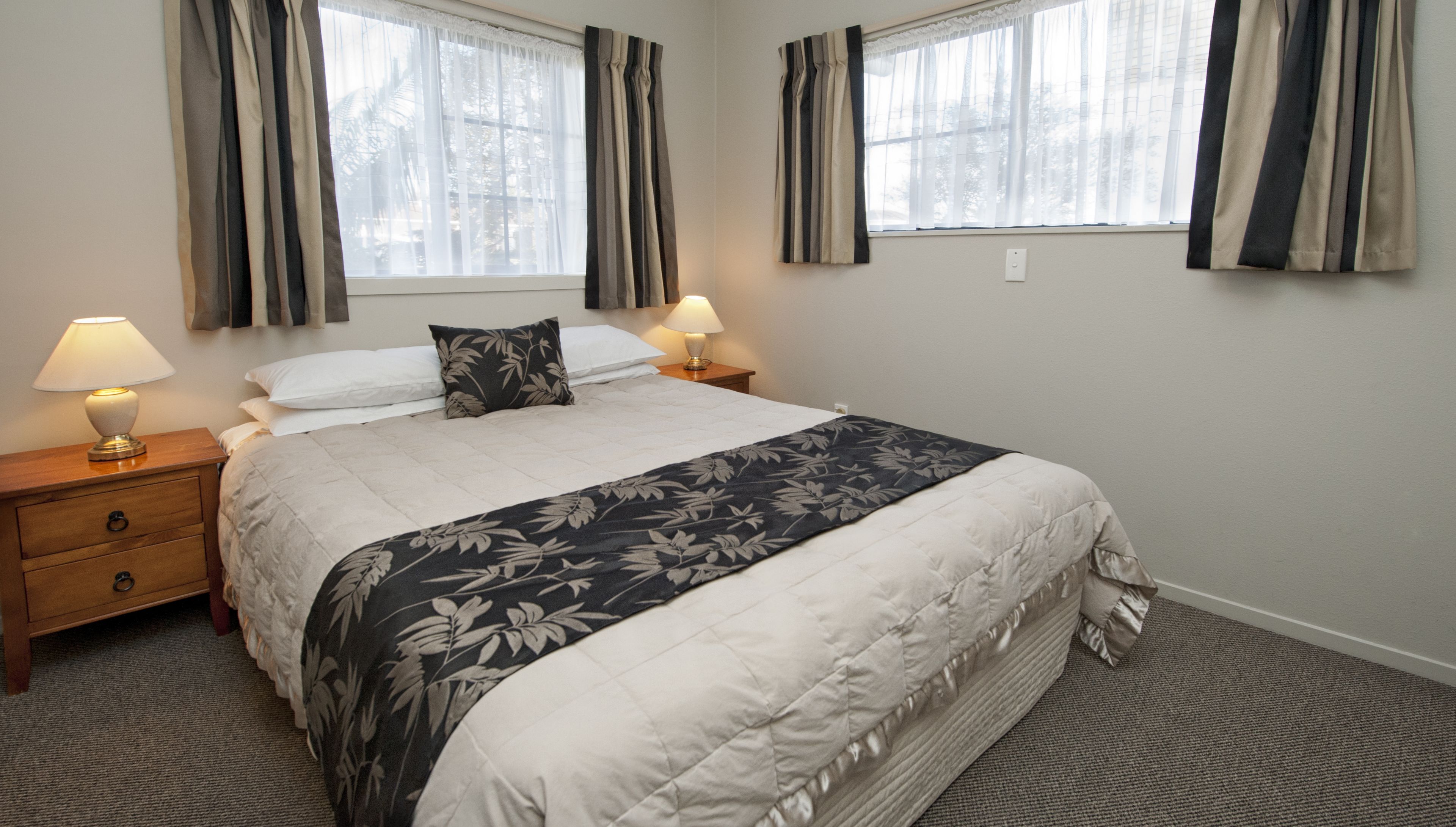 A neatly made bed with a floral bedspread, two bedside lamps, and a window with curtains.