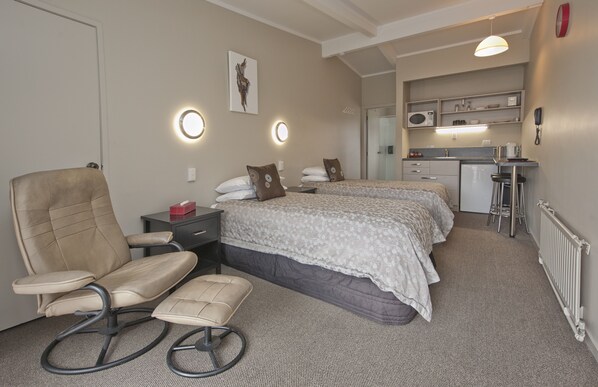 A hotel room with two beds, a desk, a chair, a small kitchenette, and a bathroom.