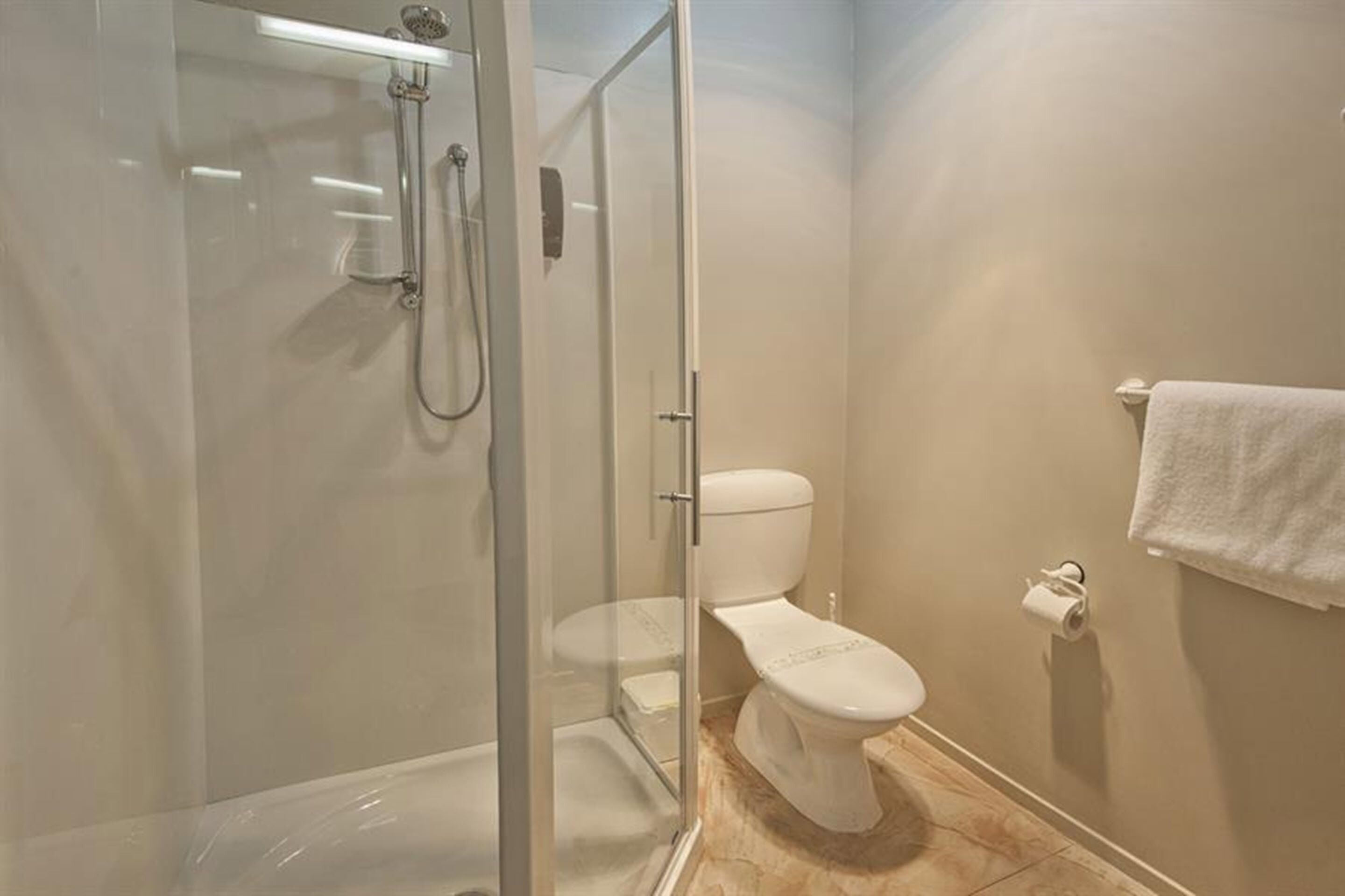 A bathroom with a glass-enclosed shower, a toilet, and a towel rack.