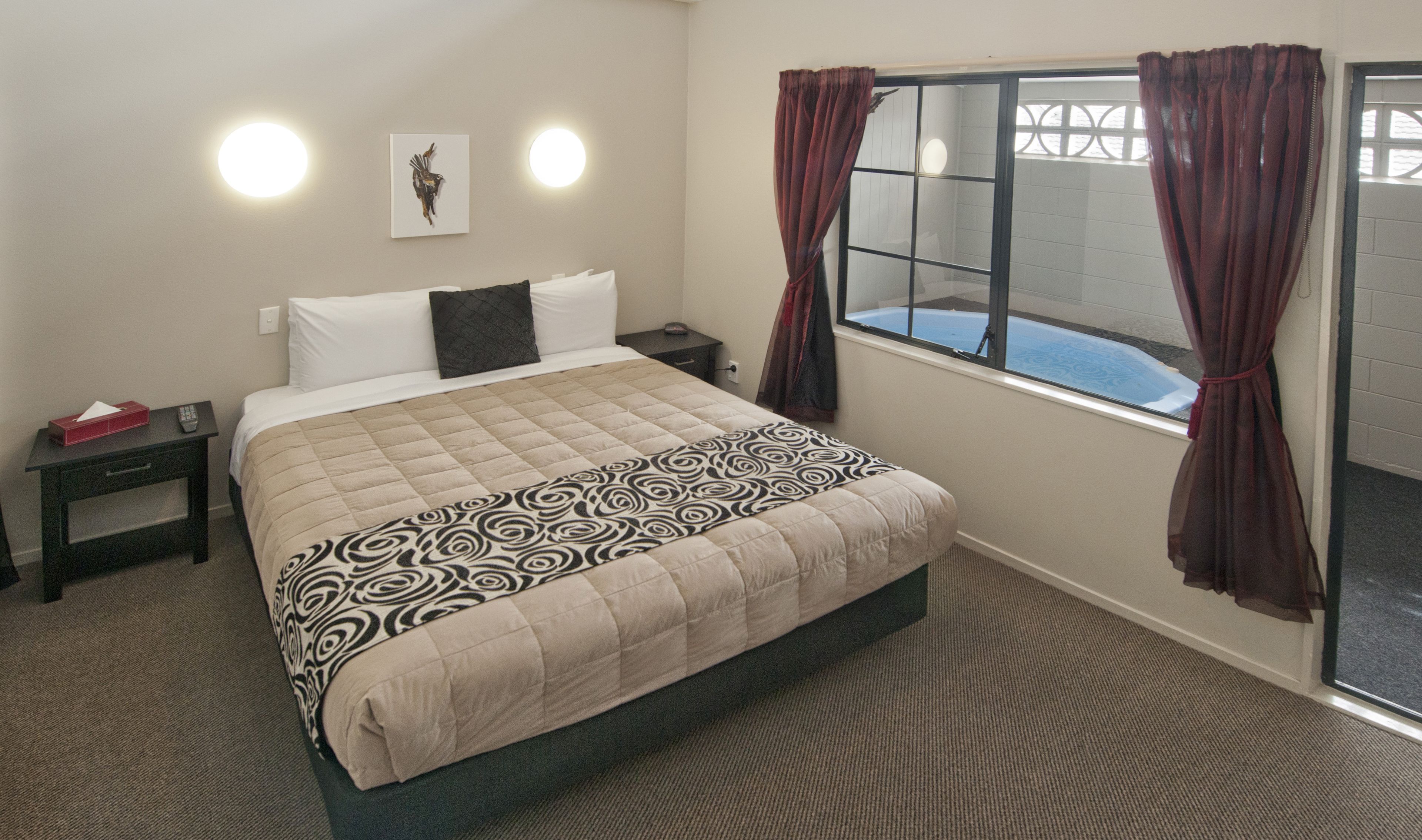 A hotel room with a bed, a nightstand, a window with curtains, and a wall-mounted artwork.