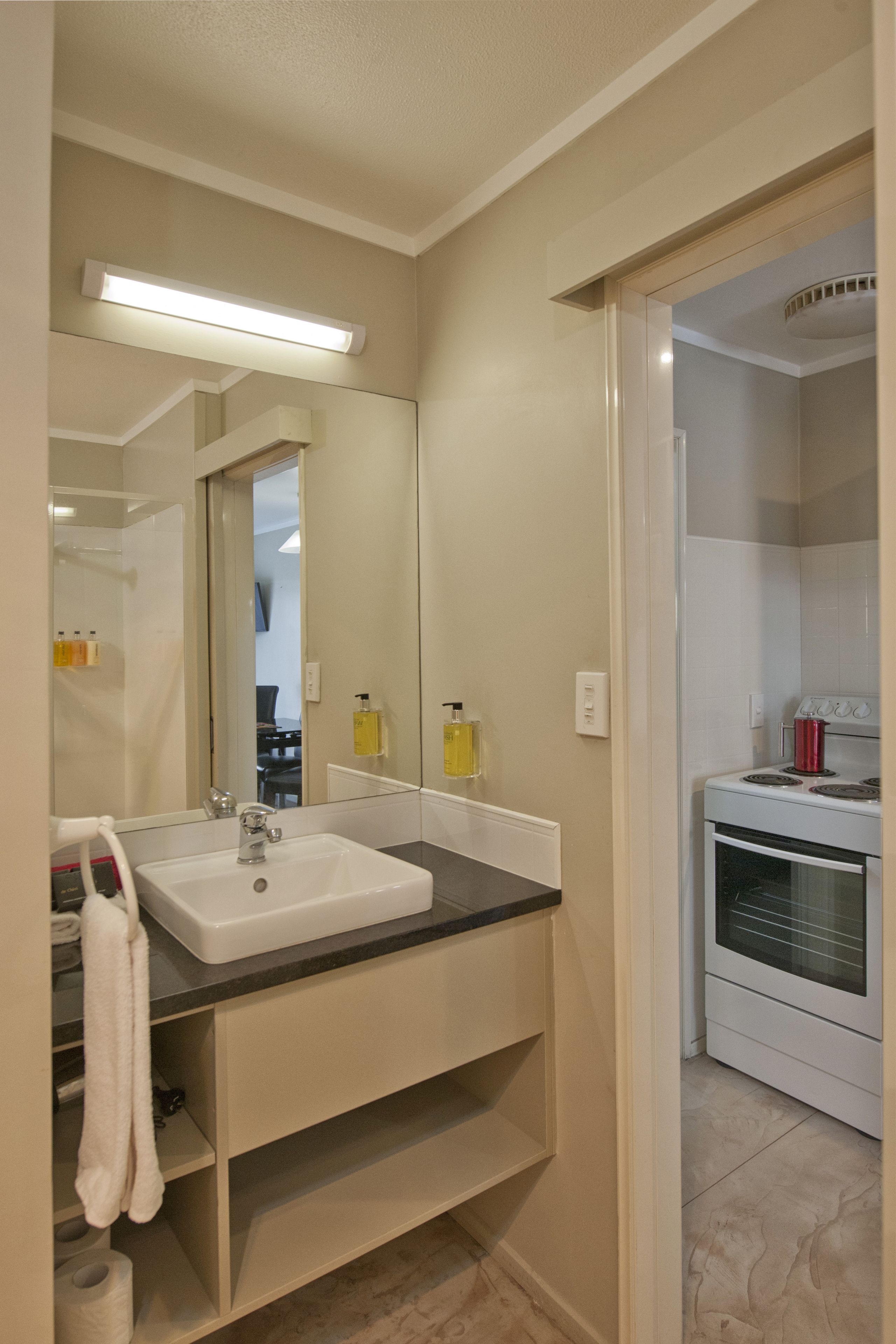 Un bagno moderno con lavandino bianco, specchio e pareti color beige. Si nota un portascope con un asciugamano bianco e un rotolo di carta igienica.