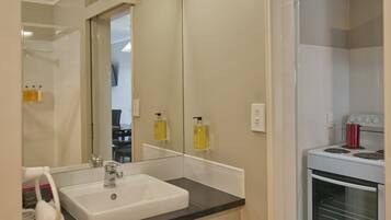 Un bagno moderno con lavandino bianco, specchio e pareti color beige. Si nota un portascope con un asciugamano bianco e un rotolo di carta igienica.