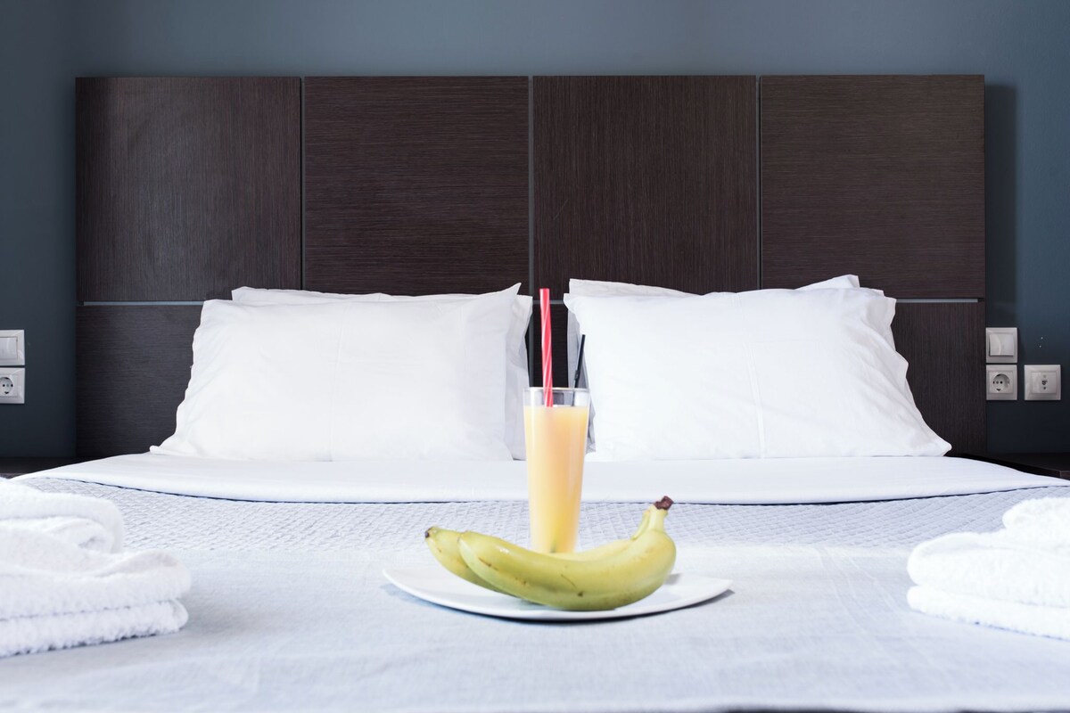 A neatly made bed with white linens, a plate with bananas and a glass of orange juice, and a dark wooden headboard.