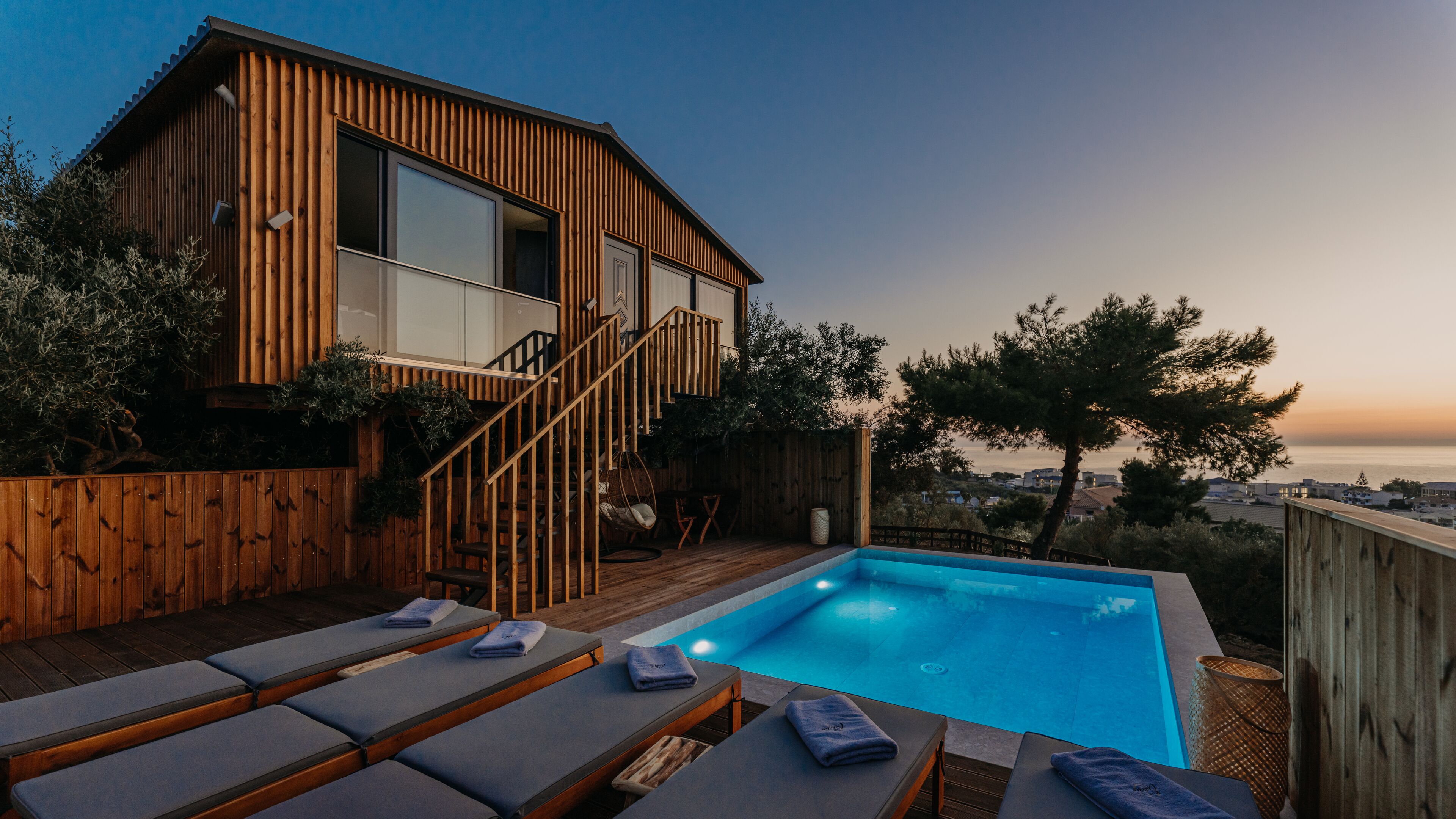 A wooden house with a pool, outdoor seating, and a view of the sea.