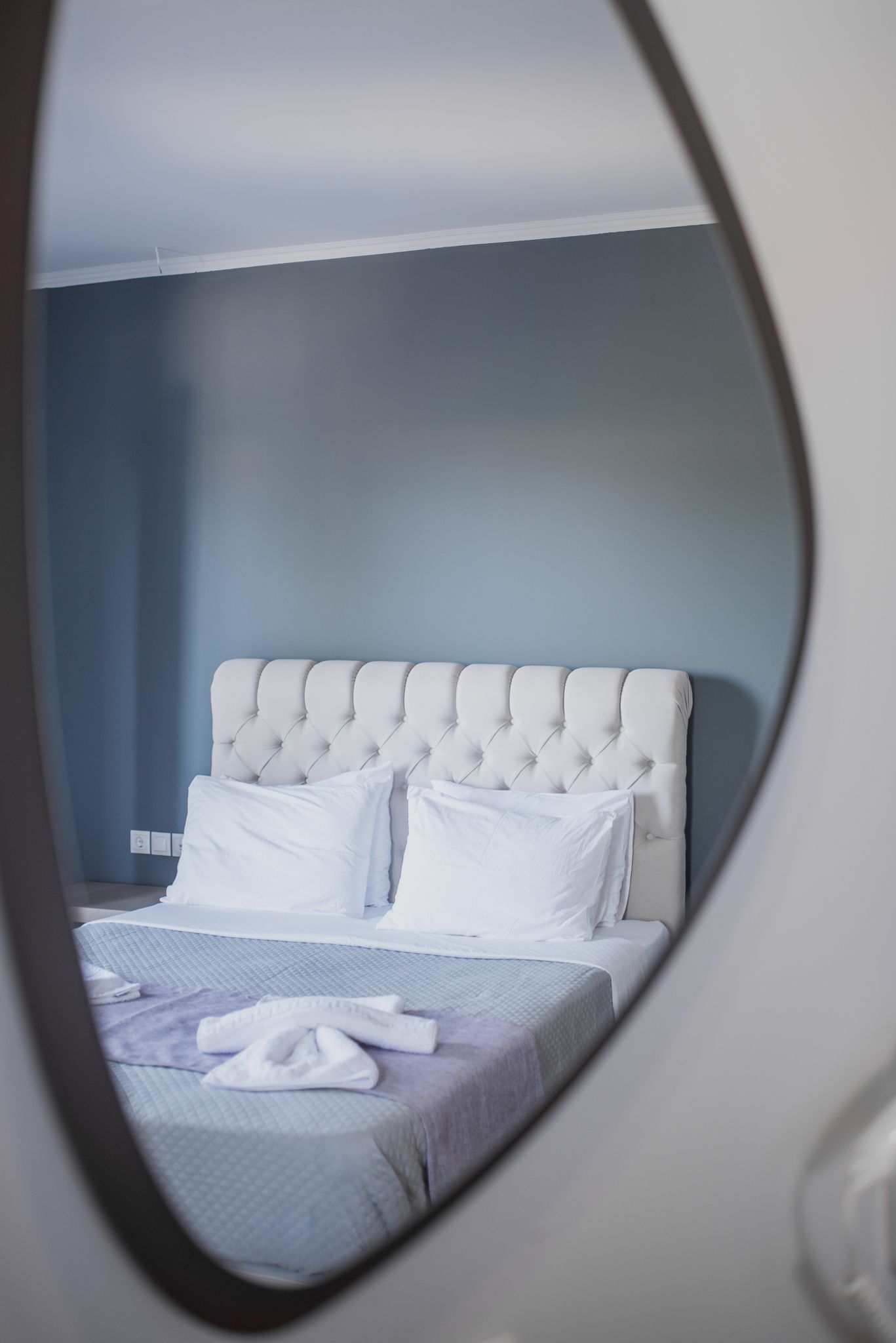 Een slaapkamer met een gestoffeerd hoofdeinde, witte beddengoed en een zichtbaar stopcontact aan de muur.
