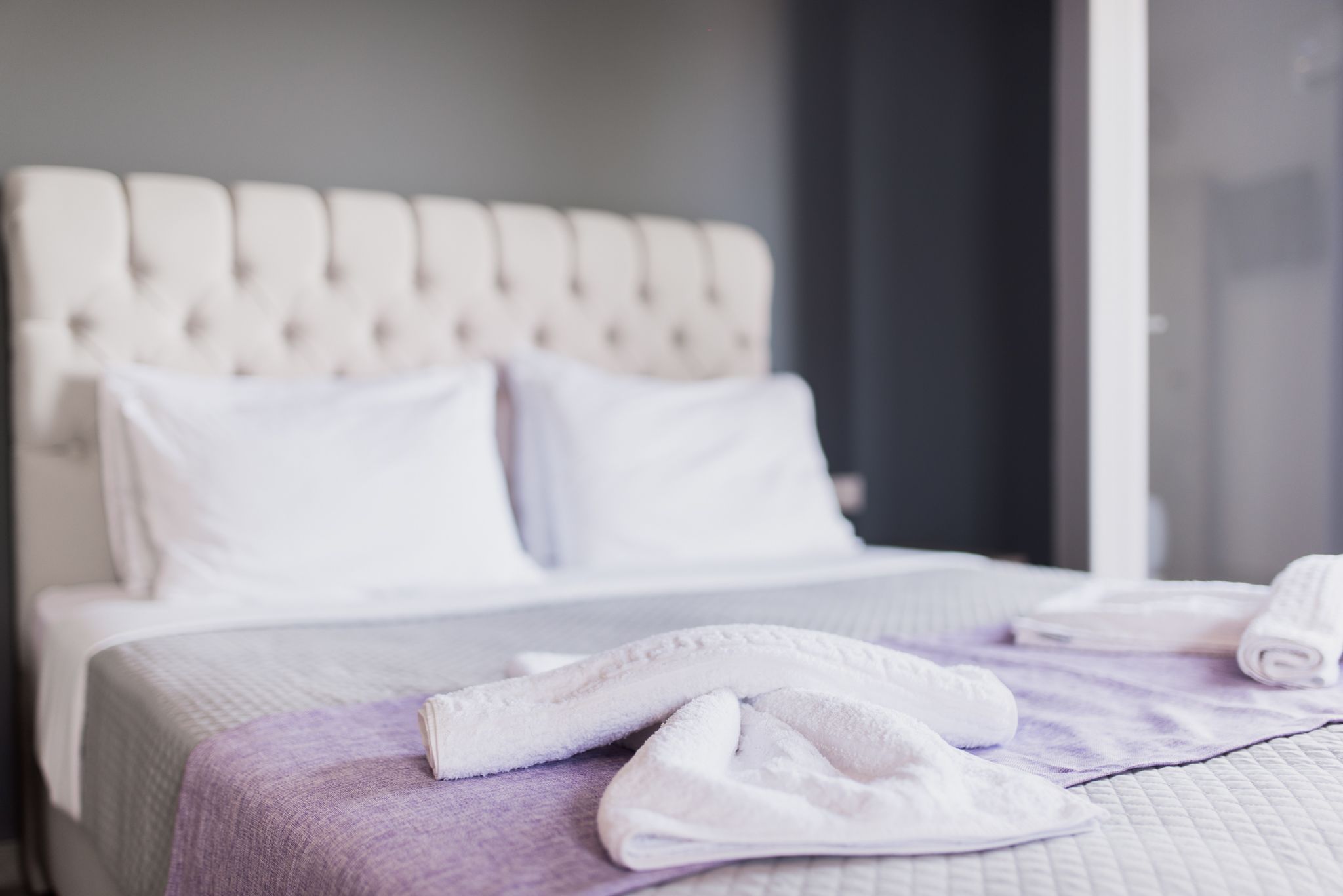 A neatly made bed with white linens and a purple throw blanket.