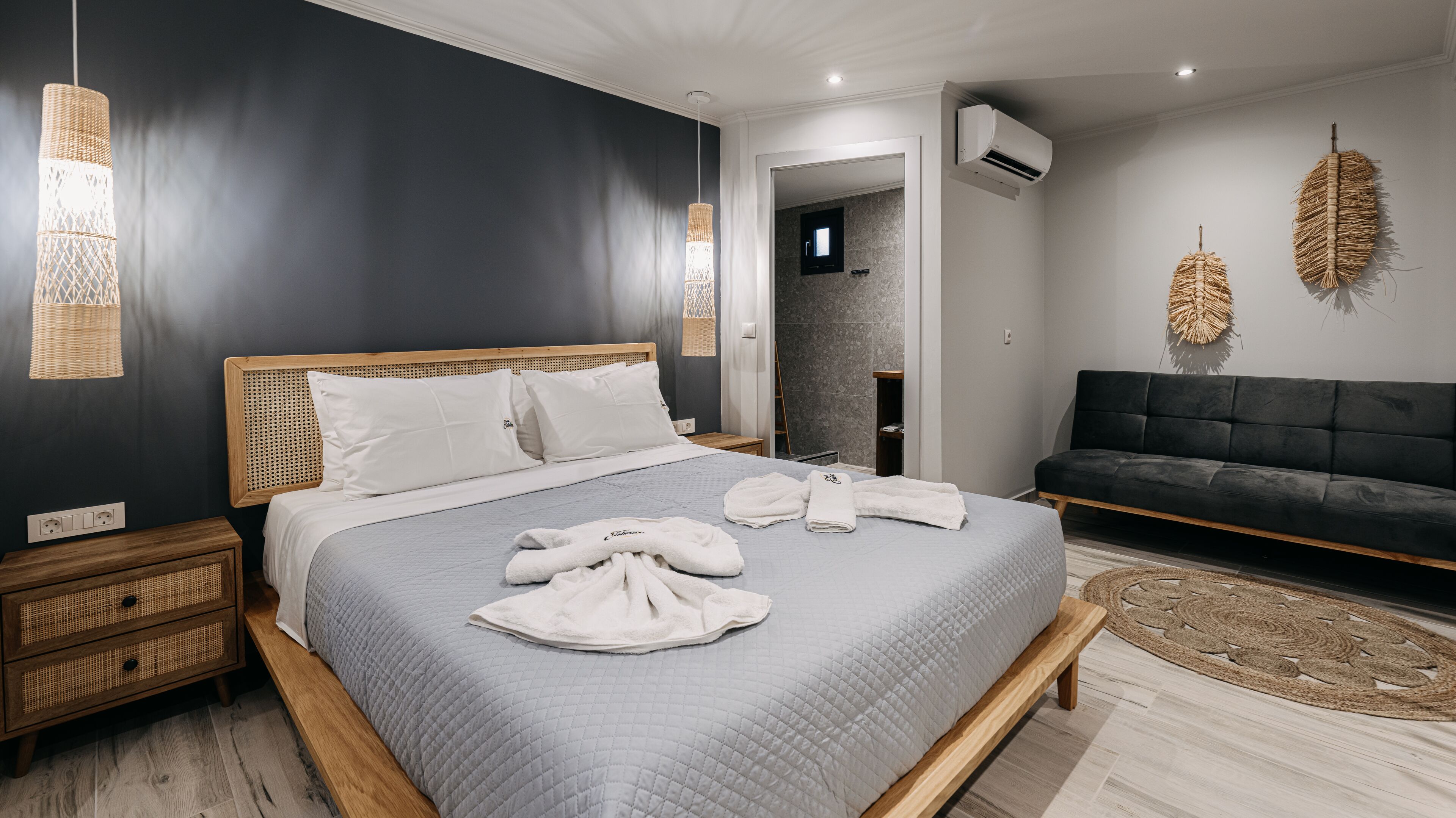 Une chambre à coucher moderne avec un grand lit, des tables de chevet, un canapé foncé et des éléments décoratifs accrochés au mur.