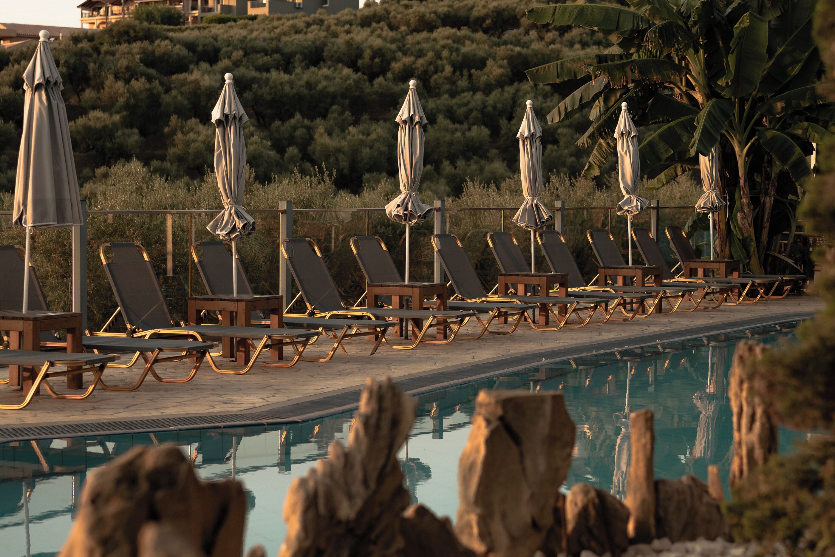 A poolside area with lounge chairs and umbrellas, surrounded by a wooden deck and a pool.