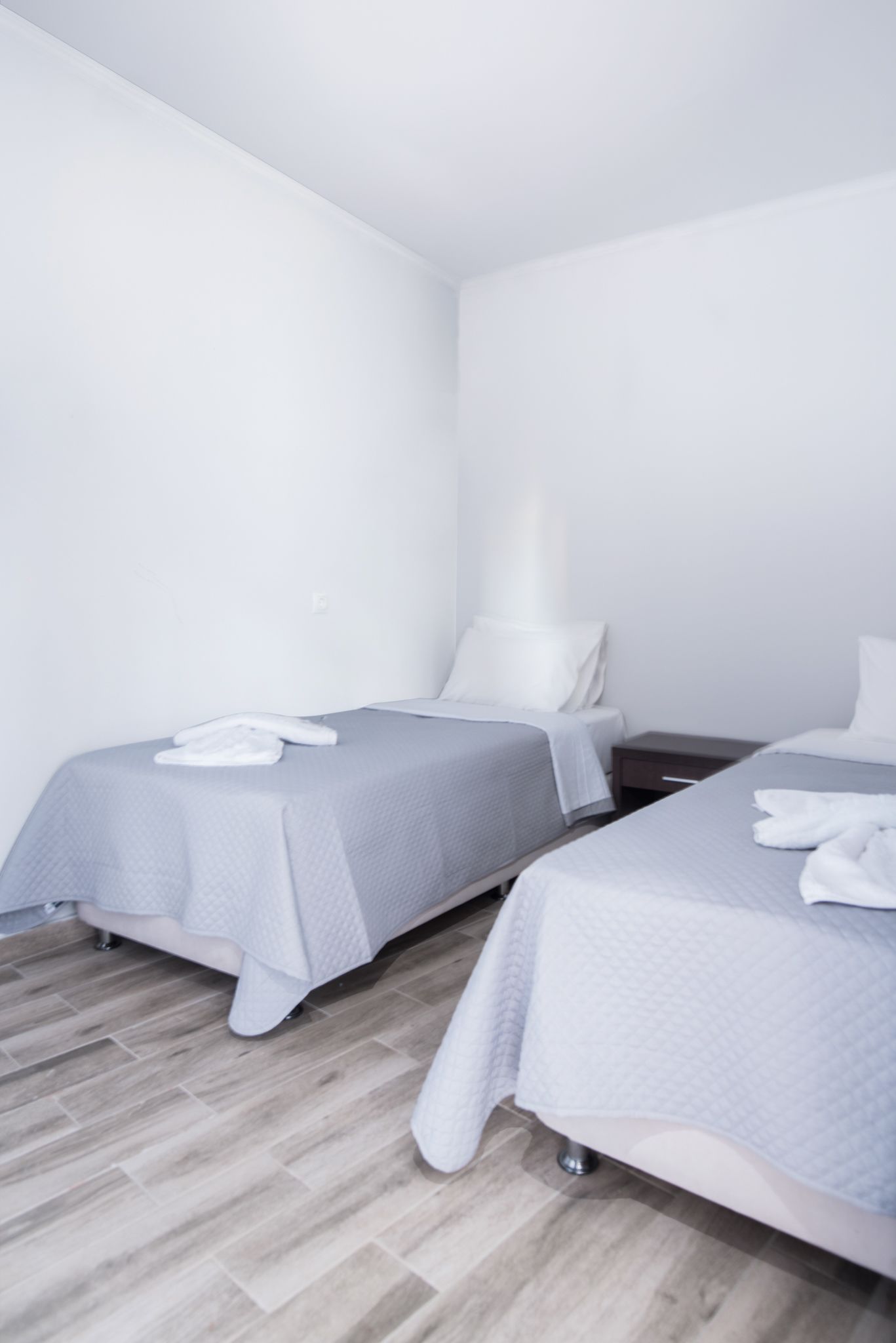 A hotel room with two single beds, a wooden floor, and a white wall.