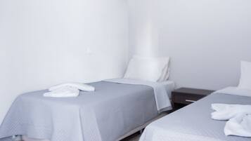 A hotel room with two single beds, a wooden floor, and a white wall.