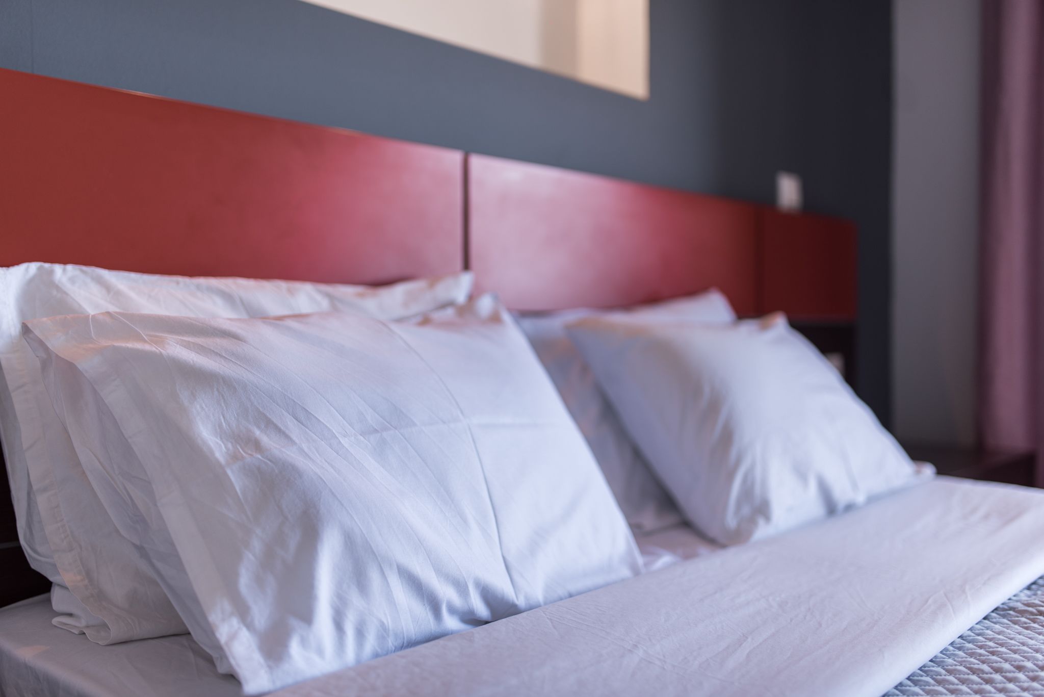 A bed with white bedding and a red headboard in a hotel room.