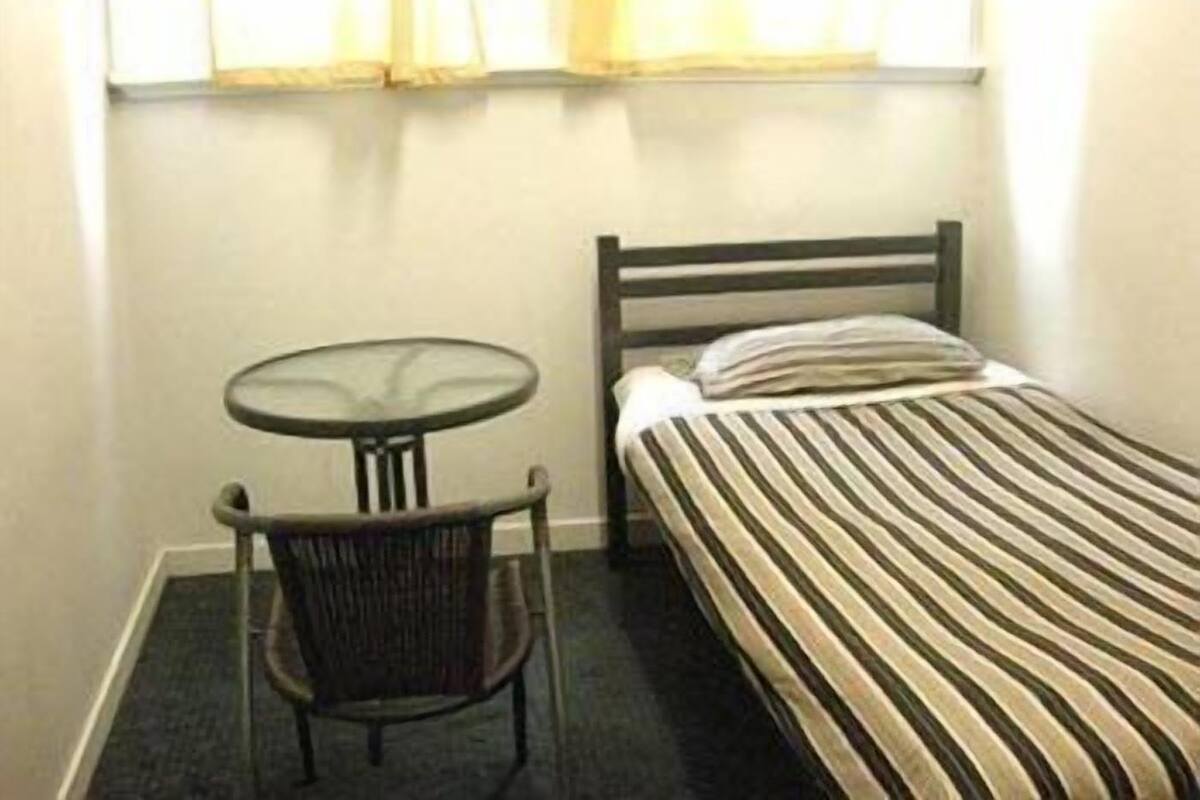 Une petite pièce avec un lit simple, une table ronde et une chaise.