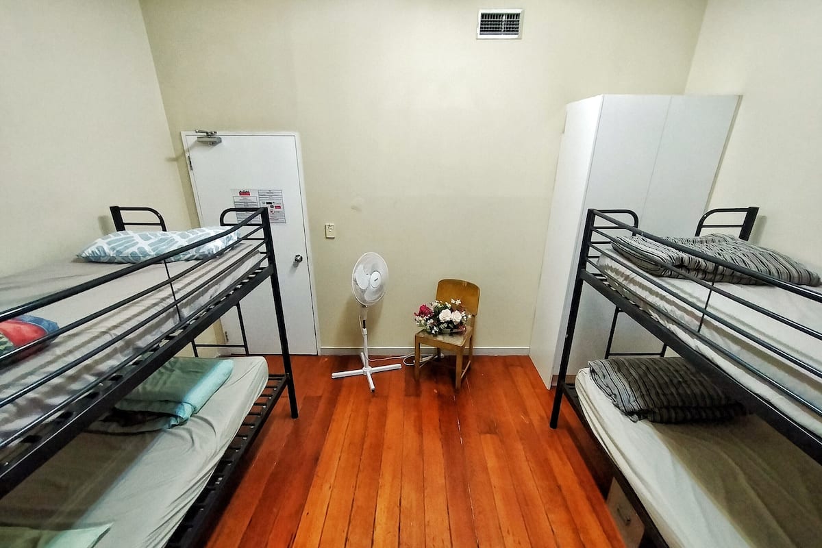 Une chambre de dortoir avec des lits superposés, un petit ventilateur, une chaise et une porte.