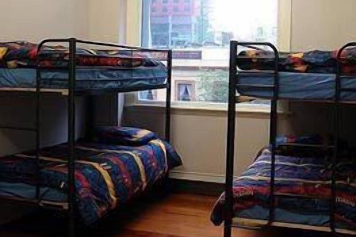 Une chambre de dortoir avec des lits superposés, une fenêtre et une vue sur les bâtiments environnants.
