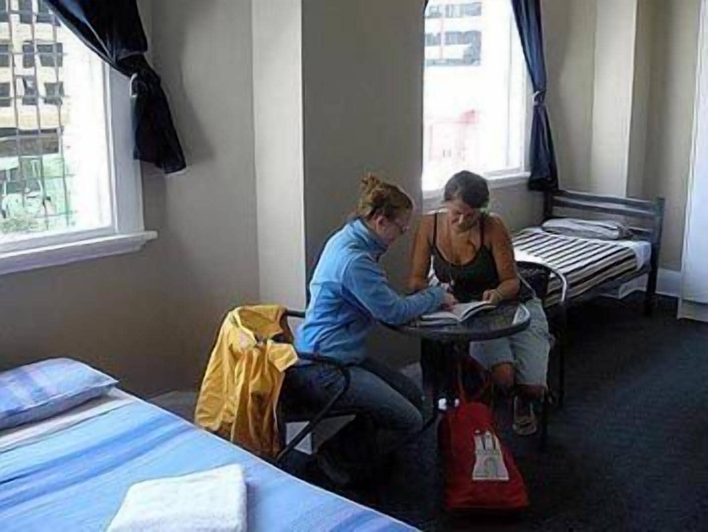 A room with two beds, a window with curtains, and a table with two people studying.