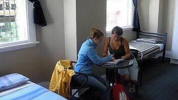A room with two beds, a window with curtains, and a table with two people studying.