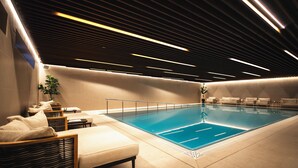 Une piscine intérieure moderne dotée d’un espace détente, comprenant des sièges et un comptoir d’accueil.