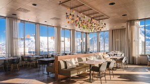 Un espace repas moderne avec une longue table en bois, des sièges confortables et de grandes fenêtres offrant une vue sur les montagnes.