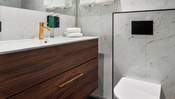 A modern bathroom with a marble wall, a wooden vanity, a white toilet, and a large mirror.