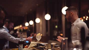 A bar setting with a bottle of Campari, a glass with ice and a lemon slice, and a person in a white shirt.