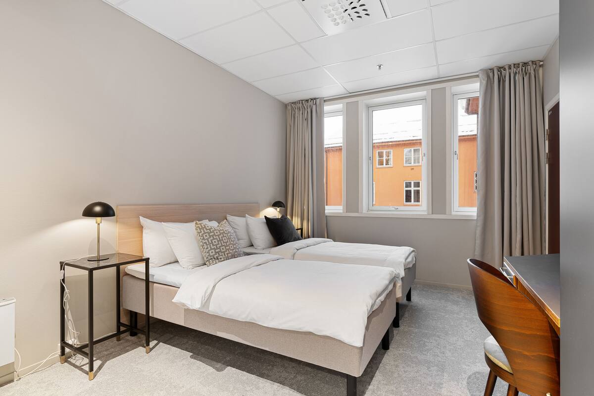 Een hotelkamer met twee bedden, een bureau en een raam met gordijnen.
