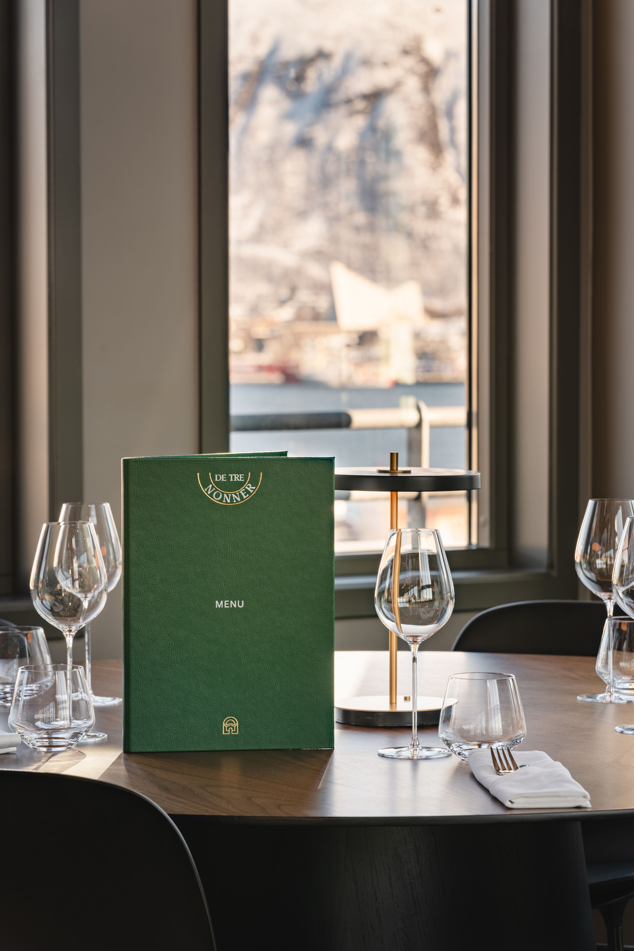 A dining table with a menu book, wine glasses, and a napkin.