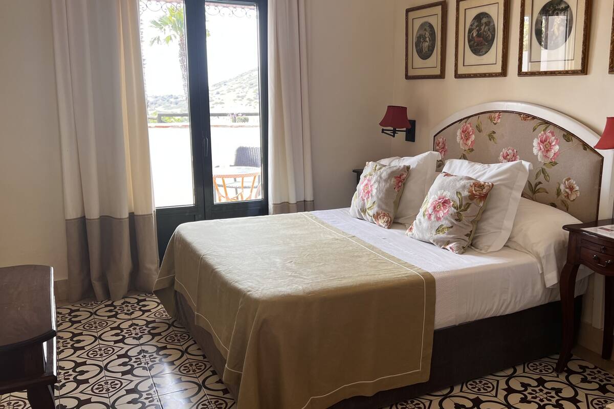 Quarto de hotel com cama, cortinas, mesa e cadeira.