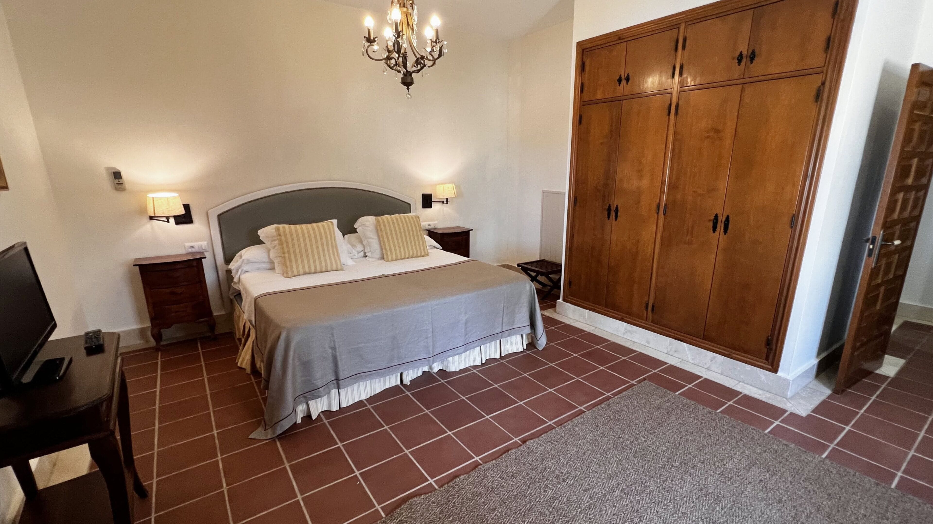 Une chambre à coucher comprenant un lit, des tables de chevet, une télévision, une armoire et un lustre.