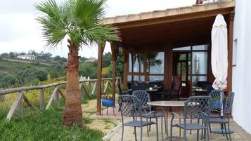 An outdoor patio with a wooden pergola, a table with chairs, and a palm tree.