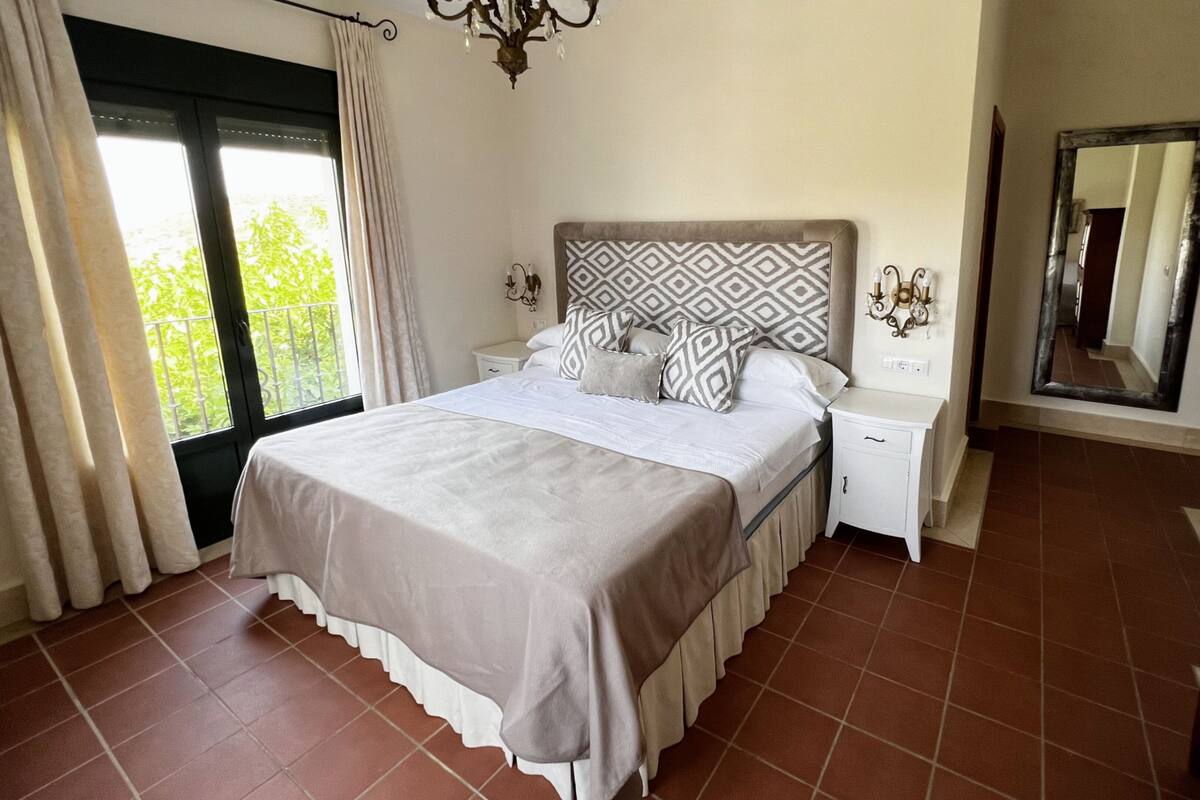 Quarto com cama, mesas de cabeceira, espelho e janela com cortinas.