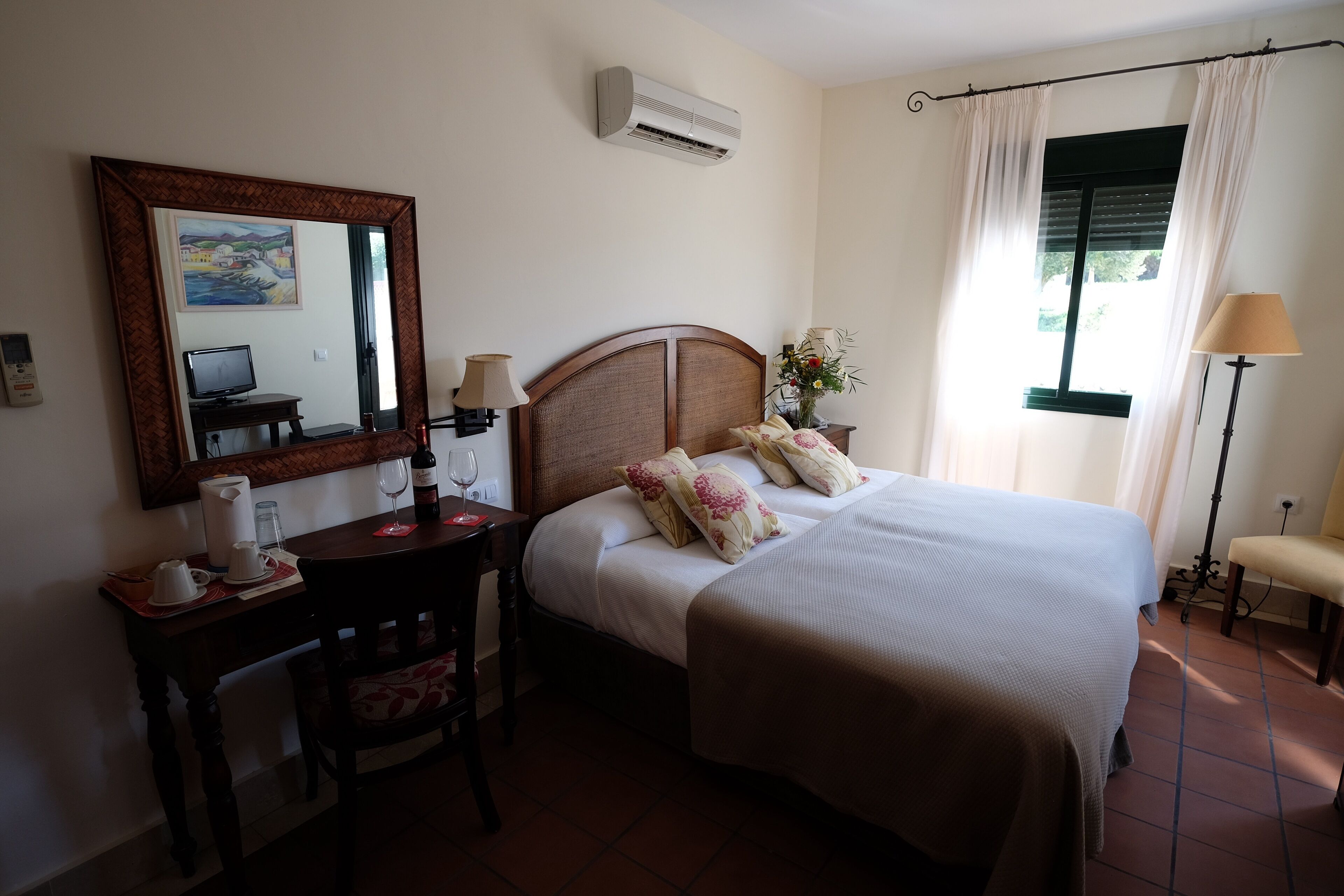 A hotel room with a bed, bedside table, chair, desk, and a large mirror.