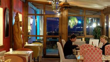 Um restaurante com paredes de madeira, janelas amplas e vista para a cidade à noite.