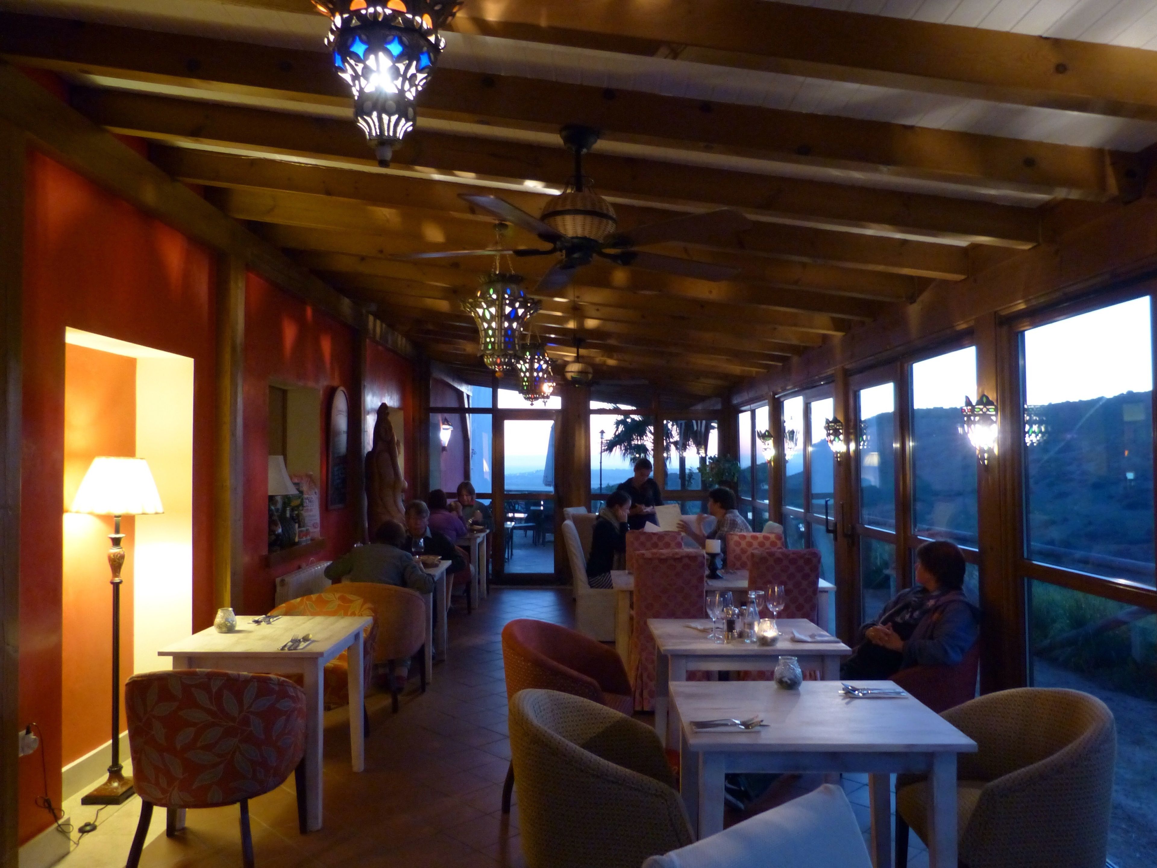 Un restaurante con vigas de madera, mesas, sillas e iluminación colgante.