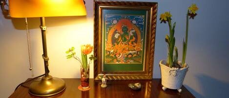 A wooden table with a lamp, a framed picture, a vase with flowers, and a potted plant.