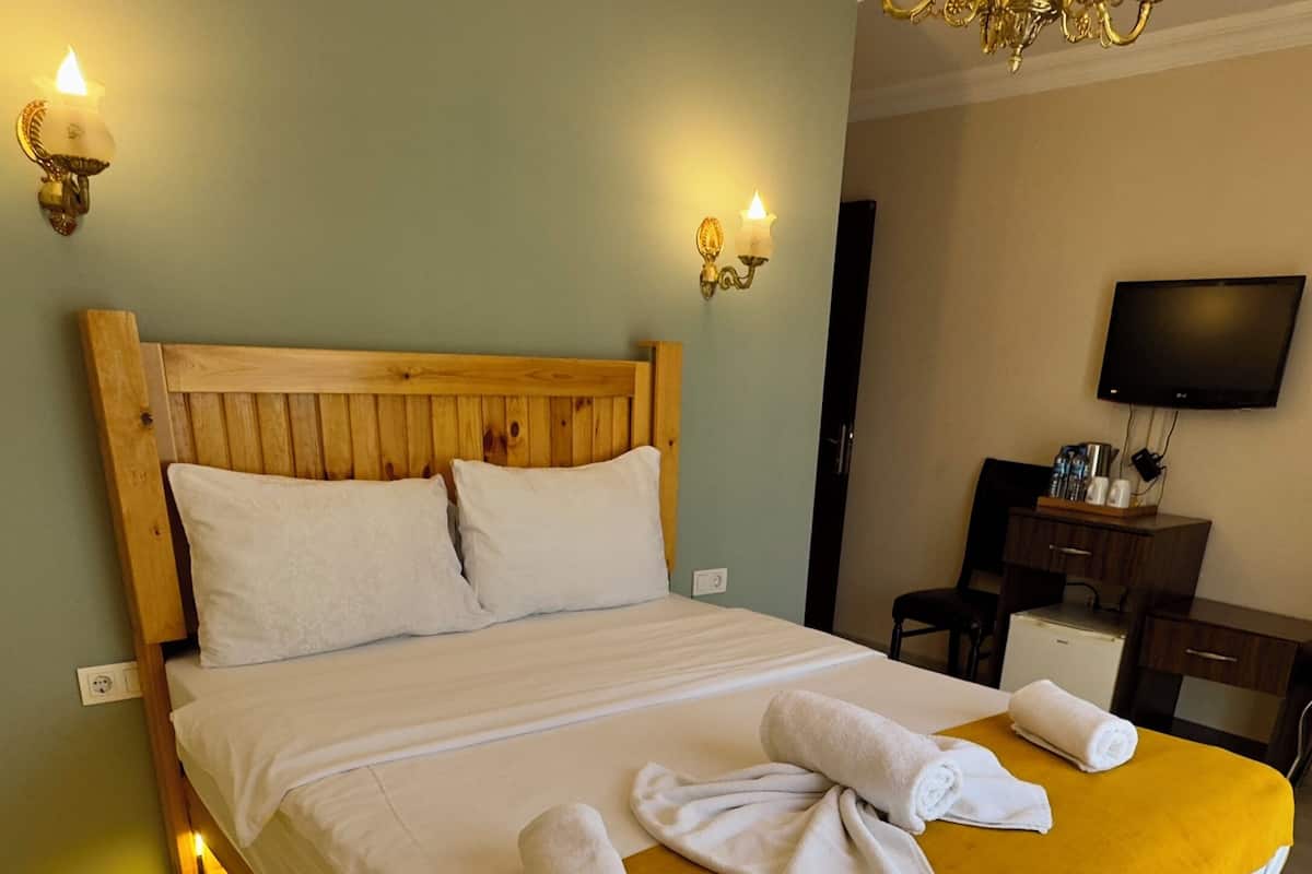 A hotel room with a wooden bed, white linens, a mustard-colored throw blanket, and two wall-mounted lamps.