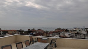 Una terraza con mesa y sillas, con vistas a un paisaje urbano costero con edificios y barcos.