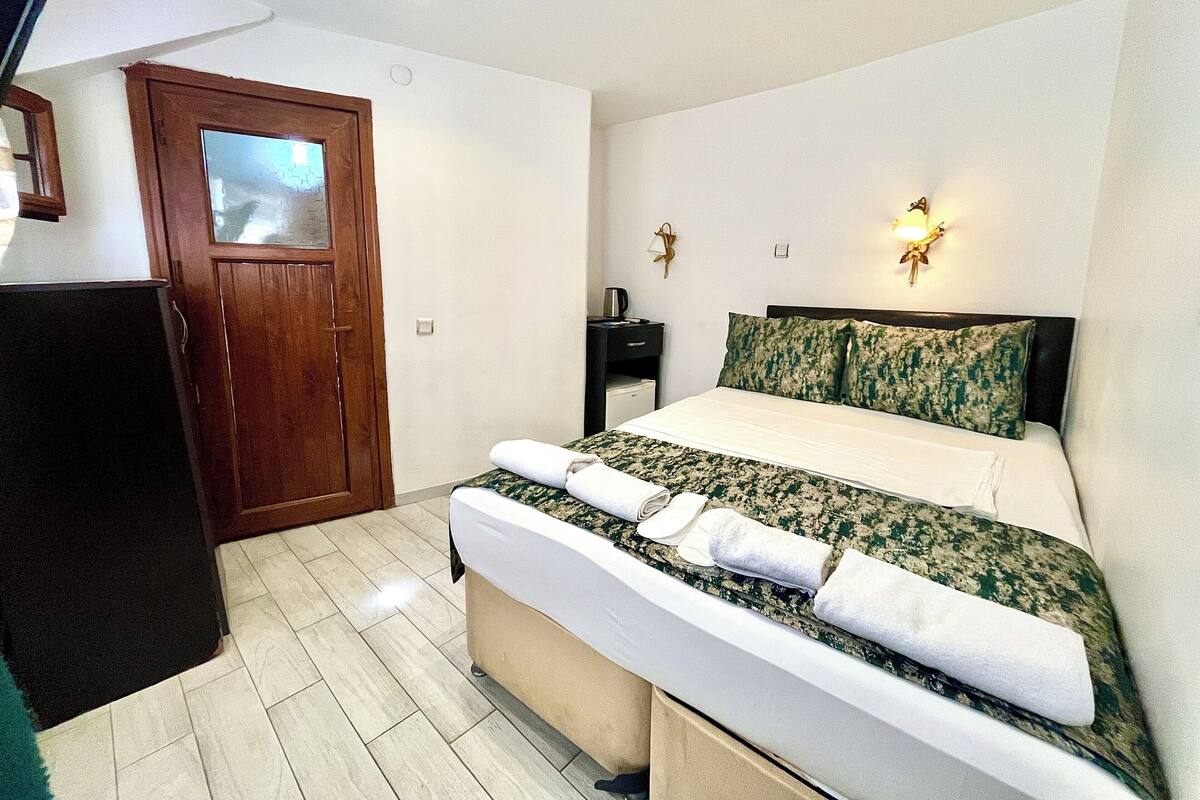 A hotel room with a bed, a desk, a chair, a wardrobe, and a door.
