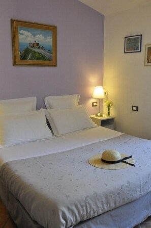 A neatly made bed with white linens, a bedside lamp, and a framed painting on the wall. - Cà du Ferrà Farm & Relax (Bonassola)