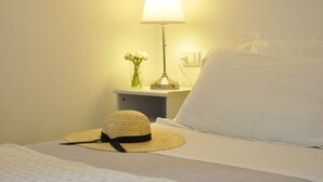 A neatly made bed with a white pillow and a straw hat placed on it. There is a nightstand with a lamp and a vase of flowers beside the bed. - Cà du Ferrà Farm & Relax (Bonassola)