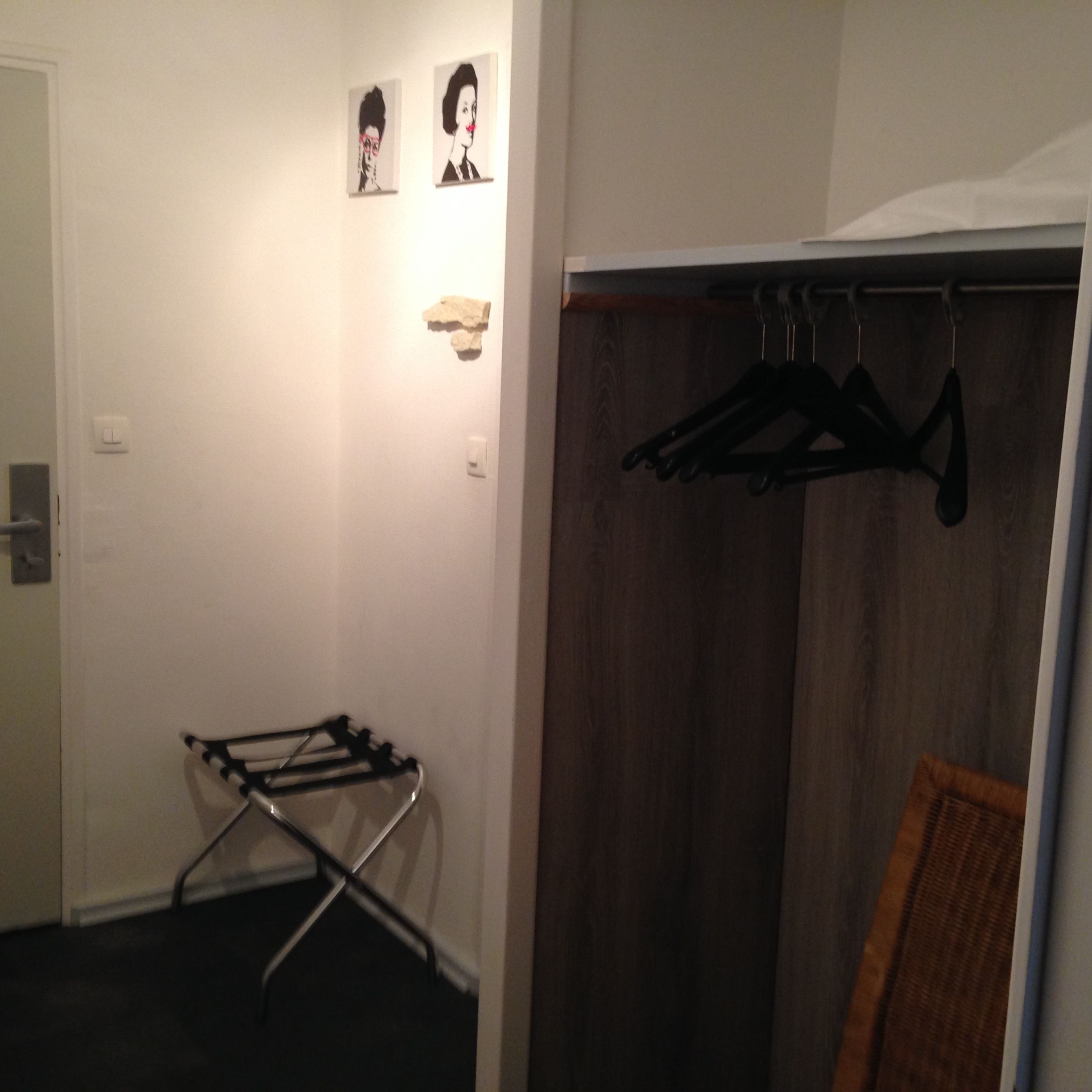Ein Zimmer mit Holztür, Wäscheständer und Kleiderschrank mit darin befindlicher Kleidung.