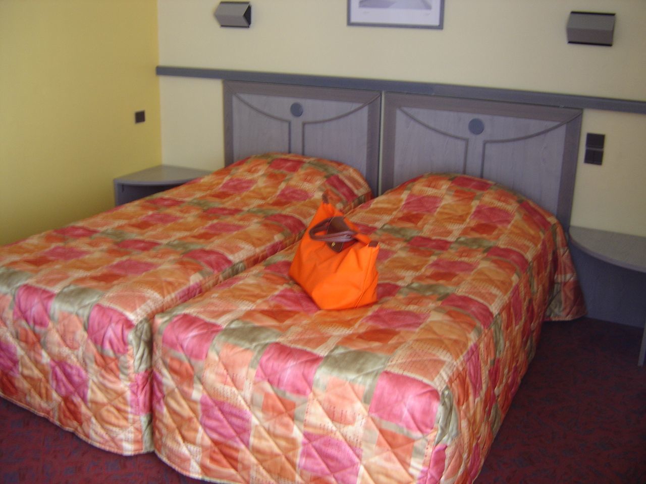 A double bed with a floral bedspread and an orange bag on it.