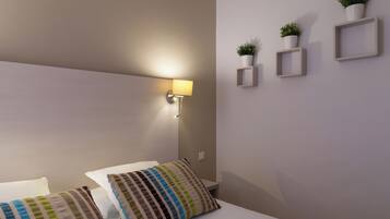 A neatly arranged hotel room with a bed, pillows, a wall-mounted lamp, and three potted plants on the wall.