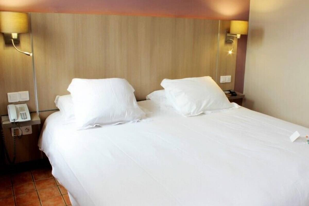 Une chambre d’hôtel avec un grand lit, deux lampes de chevet, un téléphone et une petite table.