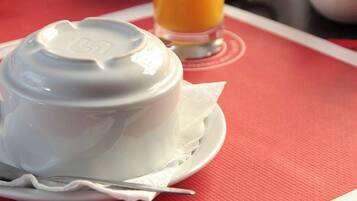 A breakfast setting with a white bowl, a glass of orange juice, and a fruit bowl in the background.