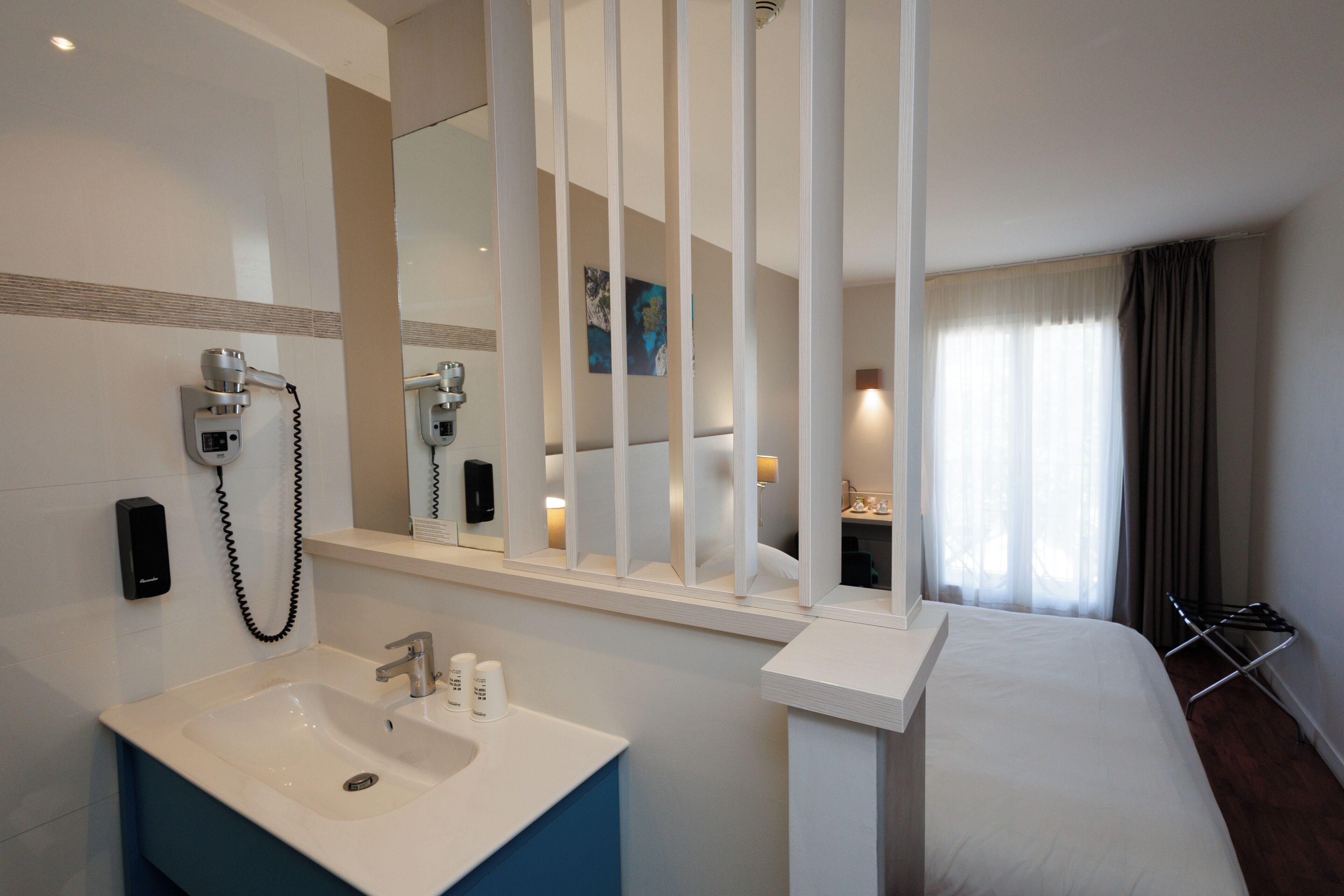 A hotel bathroom with a sink, mirror, and a bed.